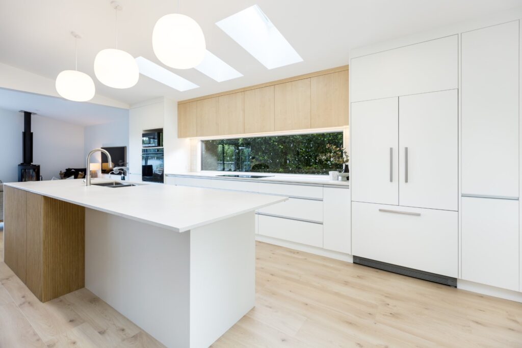 Modern white kitchen renovation in Wellington featuring skylights, timber cabinetry and a large island bench by Total Build Wellington.