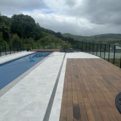 A modern outdoor pool area with tiled surrounds, timber decking, and glass fencing, reflecting architectural builds and home construction quality often included in new build homes, house plans, and design and build projects across Plimmerton Farm and Maymorn Farms.