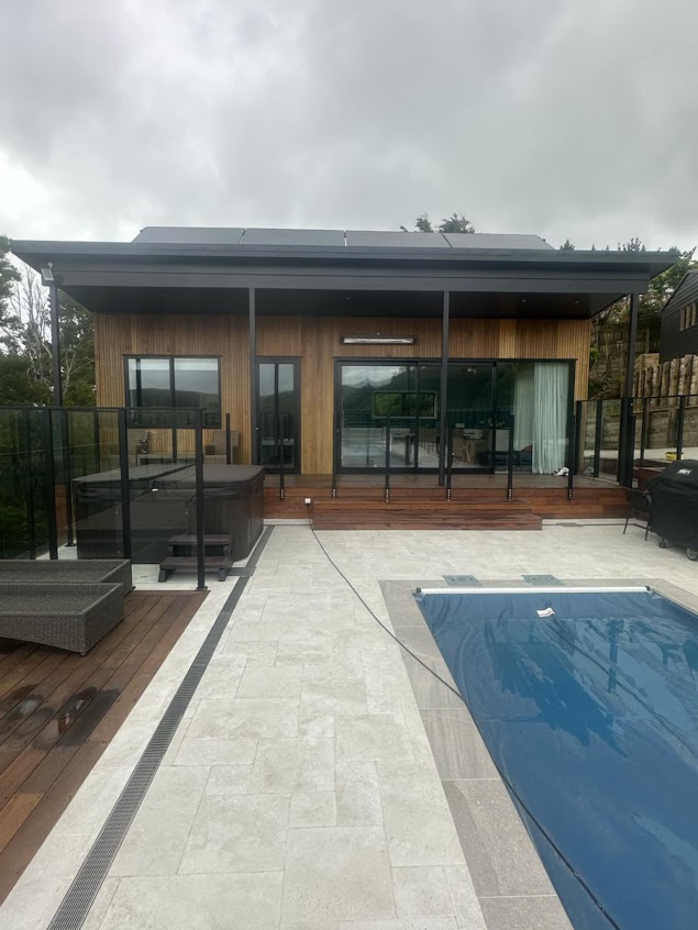 Architectural timber-clad pool house in Wellington with glass fencing and tiled outdoor area built by Total Build Wellington.