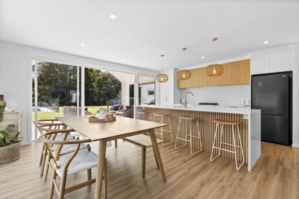 Modern open-plan kitchen and dining area in a Wellington new build home, featuring timber accents, pendant lighting and outdoor flow created by Total Build Wellington.