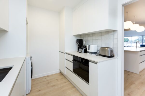 A sleek scullery featuring integrated appliances, white cabinetry, and a tiled splashback, ideal inspiration for house floorplan planning and small house design within architecturally designed homes and new builds.