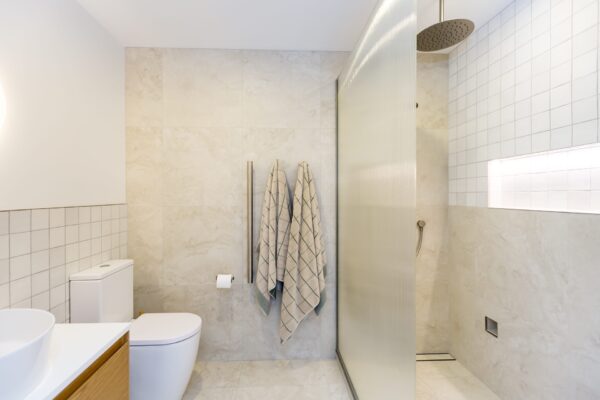 A modern bathroom featuring warm tiles, dual towel rails, and a walk-in shower, demonstrating modern bathroom layouts within architecturally designed homes and new build homes.