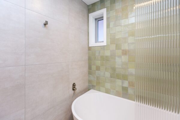 A freestanding bath against textured tiles in a modern bathroom, illustrating contemporary design choices used in new build homes, 3 bedroom house designs, and luxury bathroom concepts.