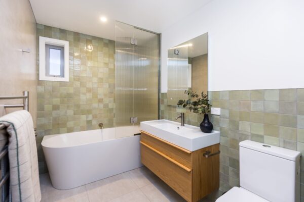 A modern bathroom featuring soft green tiles, a freestanding bath, and a sleek vanity, showcasing modern house designs and luxury bathroom styling for new build homes in areas like Plimmerton Farm or Plimmerton Heights. Ideal inspiration for house plans, small house design, and architecturally designed homes.
