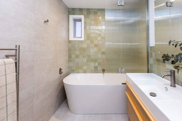 A bright modern bathroom with a tiled feature wall, freestanding bath, and glass shower screen, reflecting contemporary home construction quality within new houses and new builds. Useful visual reference for design and build projects and modern bathroom concepts.