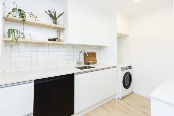 A bright modern scullery with white cabinetry, timber shelving, and tiled splashback, showcasing modern house designs and practical layouts included in many new build homes, house plans, and design and build projects in Plimmerton Farm and Maymorn Farms.